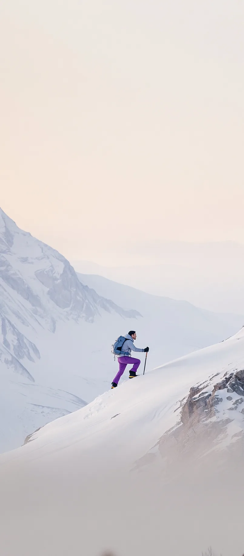 A ski tourer climbing a snow slope below an Alpine summit at dawn